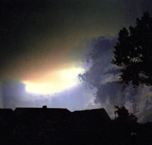 Die Silhouette eines Daches, vor dem Hintergrund eines dunklen Himmels, durch das ein helles Licht scheint.