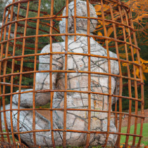 Eine männliche, sitzende Skulptur in einem rostigen Drahtkäfig.