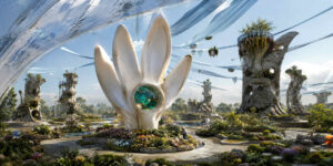 Futuristische Gartenanlage mit weißer blütenförmiger Skulptur im Zentrum eines gepflegten Parks. Transparente Netze schweben hoch über den Wegen und verbinden ungewöhnliche Türme. Menschen bewegen sich zwischen Blumenbeeten und Wasserflächen. Die helle Szene vermittelt Harmonie zwischen Natur und Architektur.