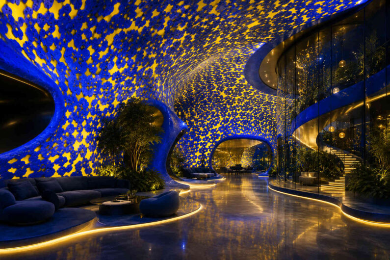 Geschwungener Innenraum wird von einer leuchtenden blau-goldenen Decke mit sternartigen Mustern überzogen. Sanfte Lichtlinien führen durch Lounges, Treppen und bepflanzte Bereiche. Die Architektur verbindet Eleganz, Komfort und visionäres Design. Spiegelnde Oberflächen verstärken die warme und zugleich kosmische Atmosphäre.